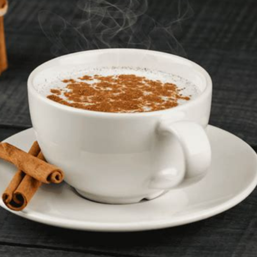 a white mug of salep that is dusted with cinnamon and a couple of cinnamon sticks on the side. 