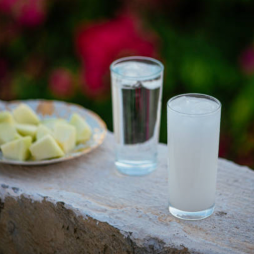 A small plate of fruit, a glass of raki and a glass of water on a stone wall.