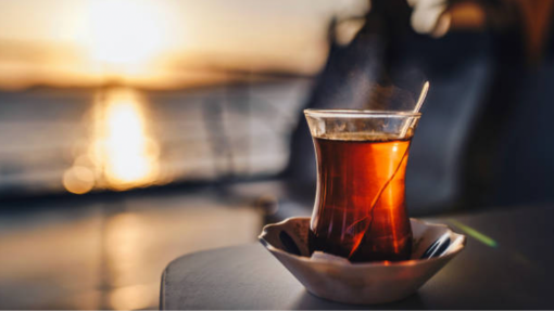Turkish Tea served in a tulip shaped glass on a table with a beautiful sunset in the background. 