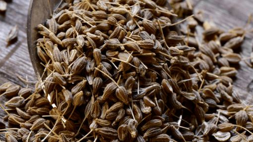 Anise seeds spilling out of a wooden spoon on a table