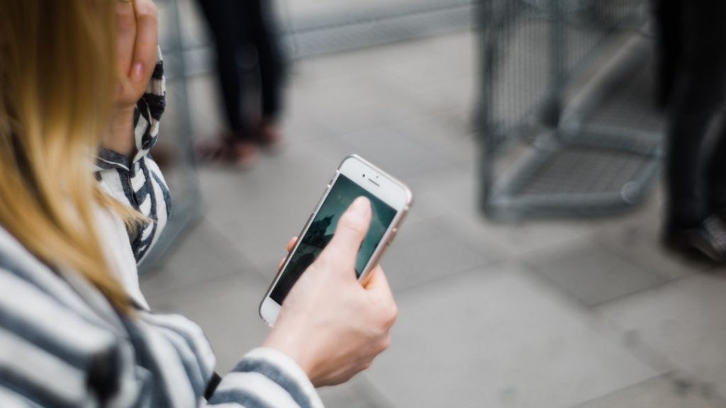 woman playing on her phone outside on a stone walkway. 