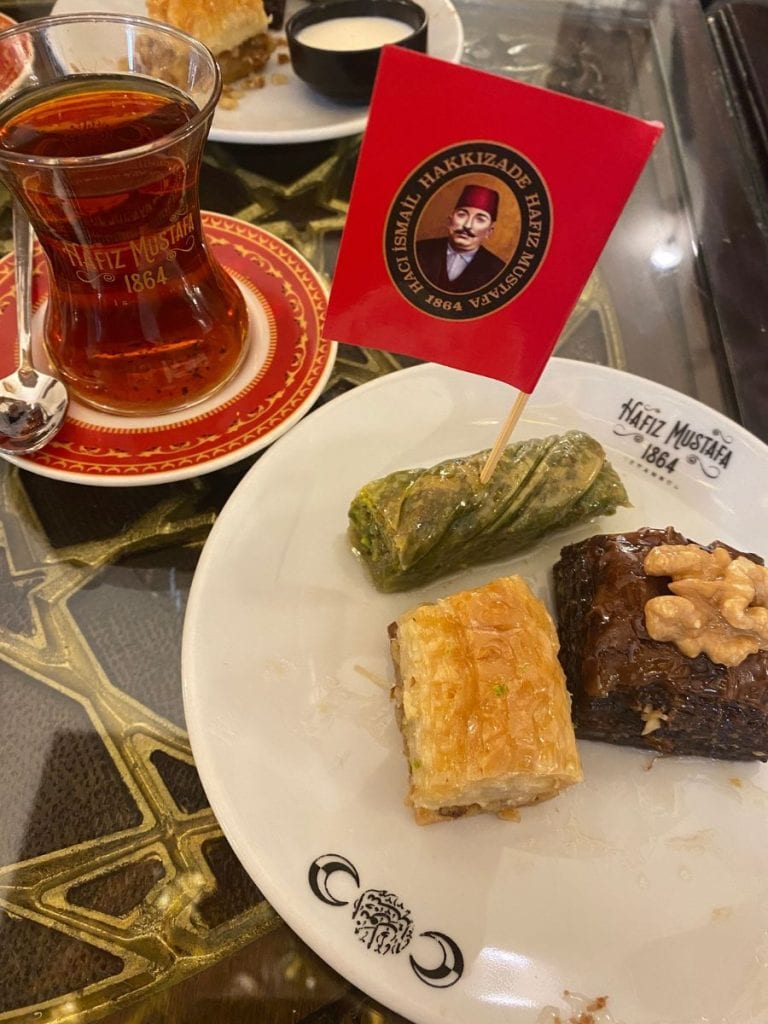 A tray of three different baklava and a turkish tea. Pistachio baklava, Tratitional Turkish Baklava, and Chocolate Baklava
