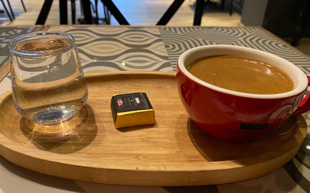 Turkish Coffee  on a wooden platter with a small chocolate and a small glass of water. 