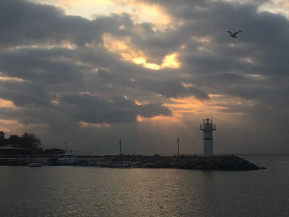Sunset on the coast of Istanbul with a lighthouse in the background and the sun peaking through the clouds