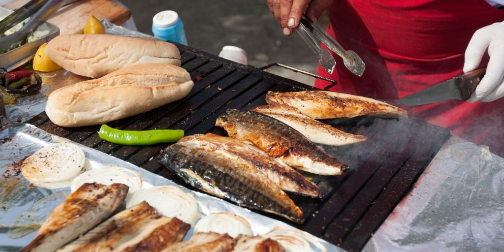 person grilling fish and bread and onions on an outdoor grill for fish sandwhiches. 