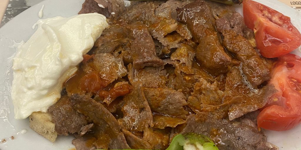 Iskender kebab on a plate drizzled with butter and garnished with yogurt, tomatoes and green peppers.