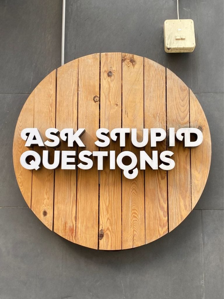 Ask stupid questions as a quote attached to a wooden panel circle