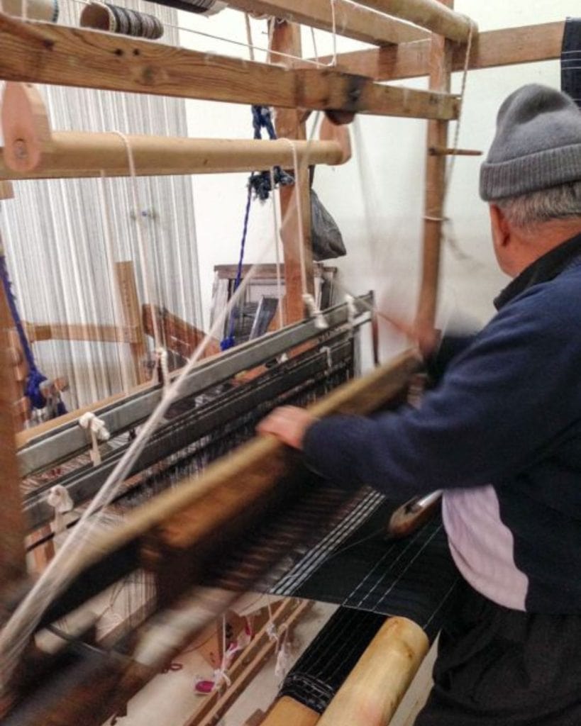 An older weaver artisan working on the loom with a flat woven piece