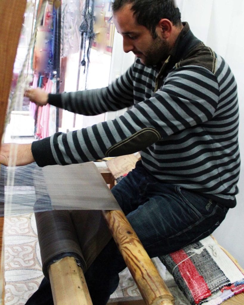 A weaver working on a peshtemel while seated at a loom