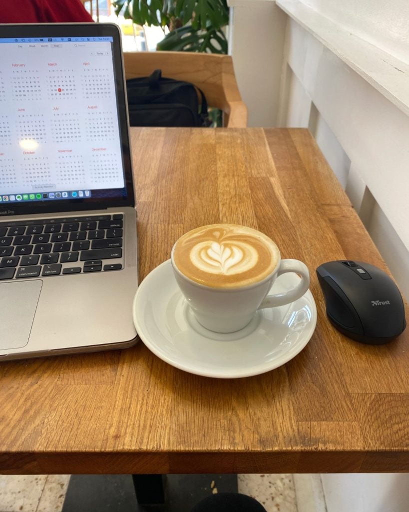 A cappuccino, computer and a mouse on a small table at a local cafe where I work sometimes. 