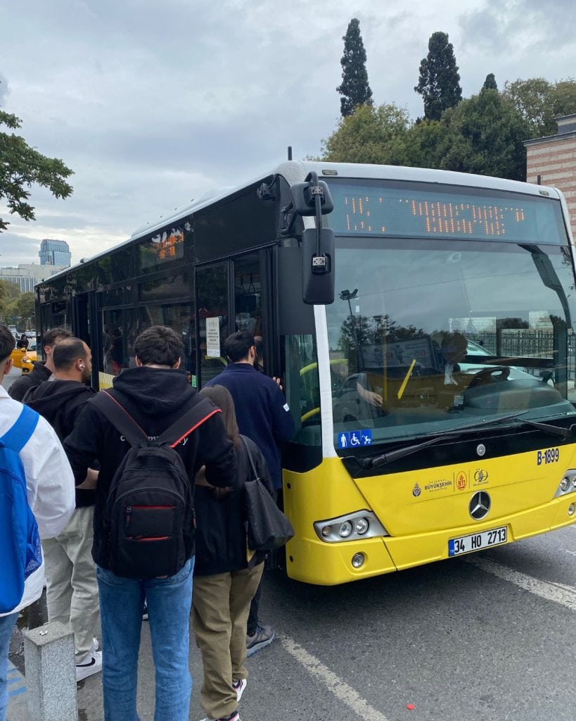 People waiting to board a yellow city bus in Istanbul.