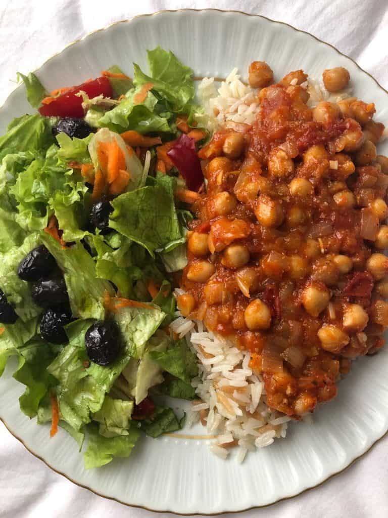 chickpeas over rice with a side salad on the same white plate.