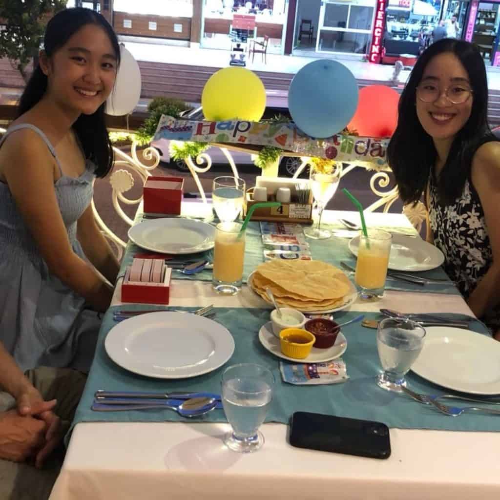 Two young women sit at a restaurant table decorated with birthday balloons.