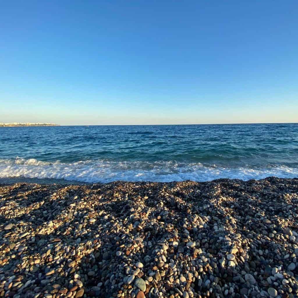 A pebble beach at Konyaalti, Antalya with white waves and the Mediterranean Sea in the distance.