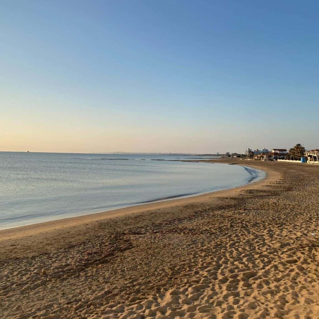 Sandy Lara Beach with a calm Mediterranean Sea and buildings in the background.