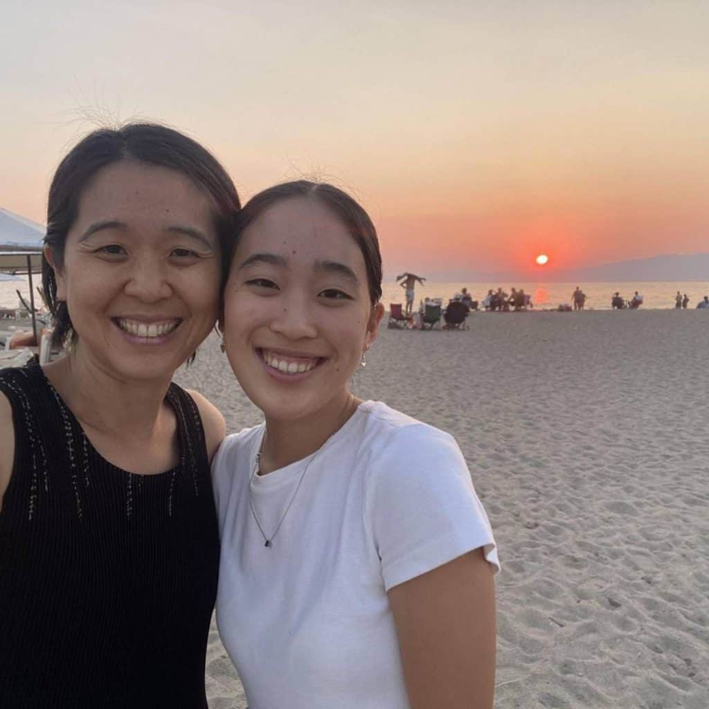 A woman and her daughter pose in front of the sunset over a sandy Oren Beach.