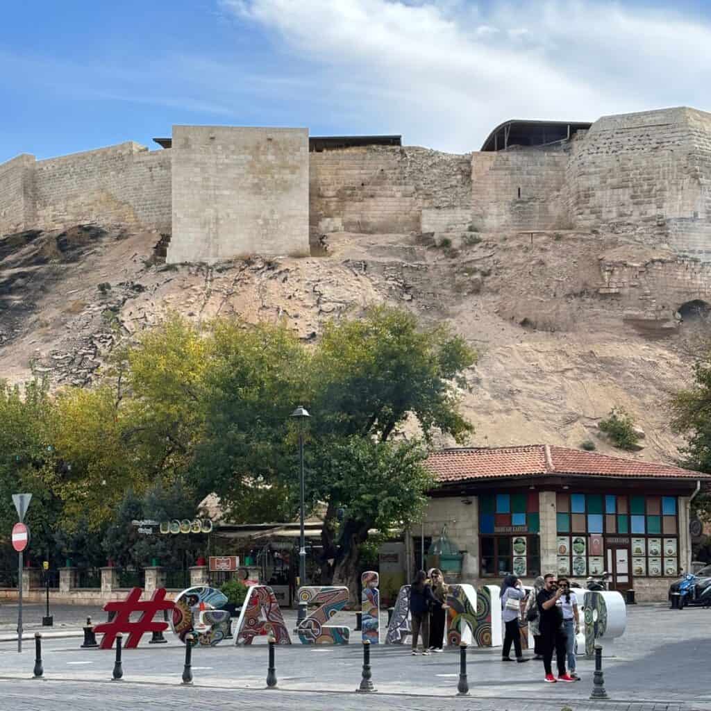 A view of the newly reconstructed Gaziantep Castle, with people taking touristic photos at the base of the hill.