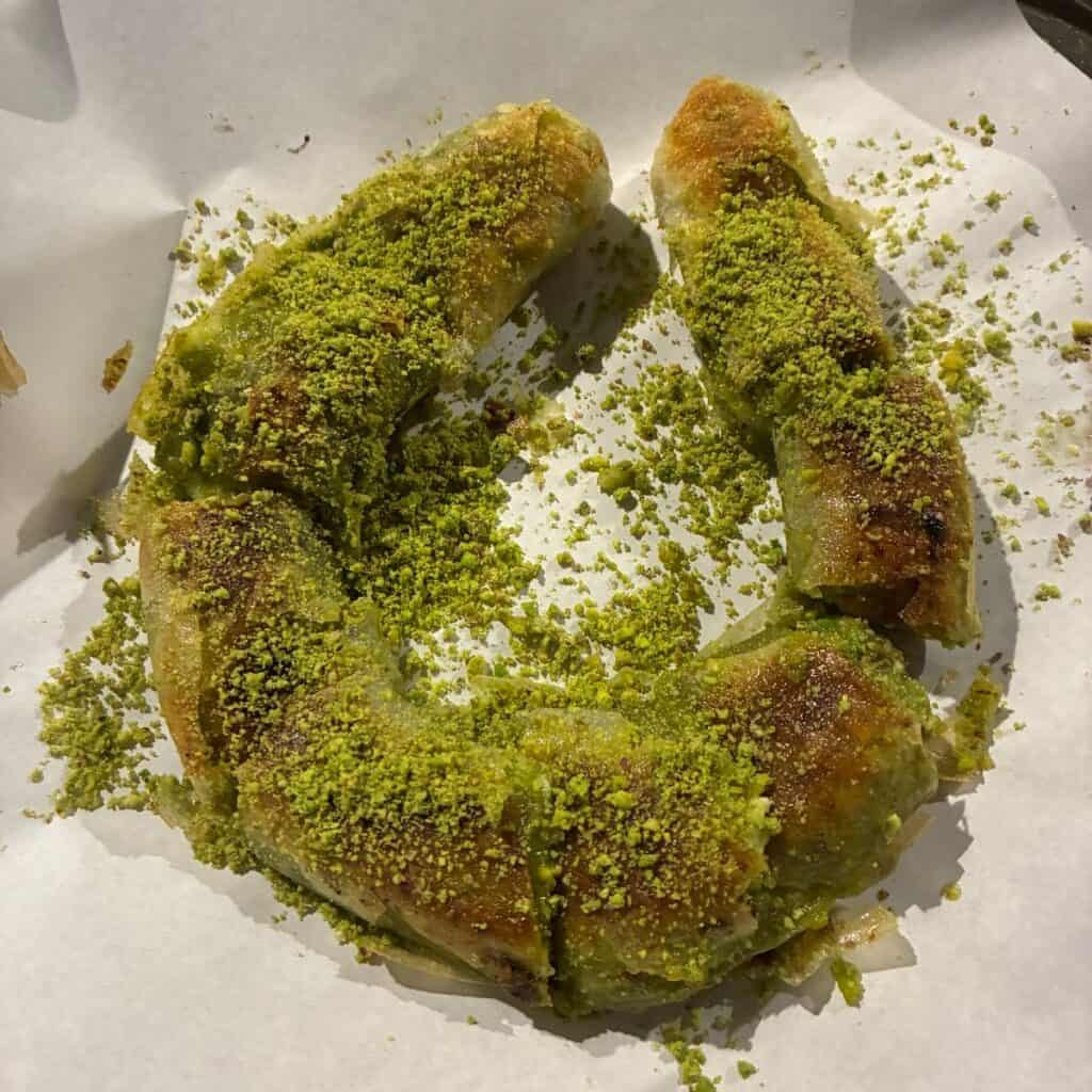 A Turkish dessert in the shape of a circle, with flaky pastry and crushed pistachios sprinkled on top.